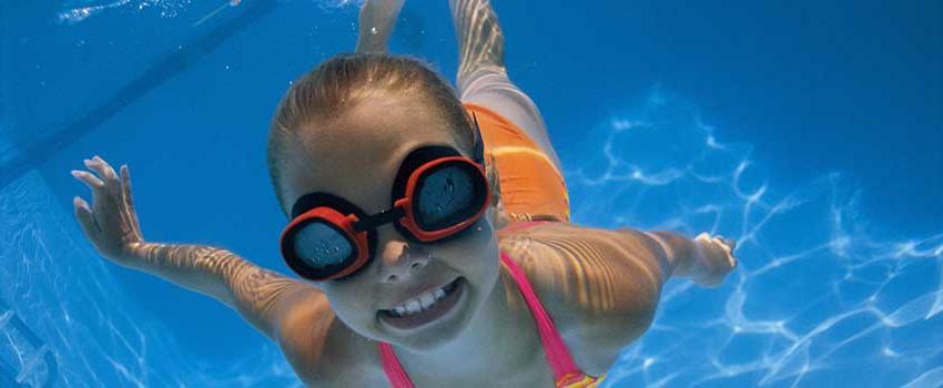Girl in goggles and smiling swimming underwater.